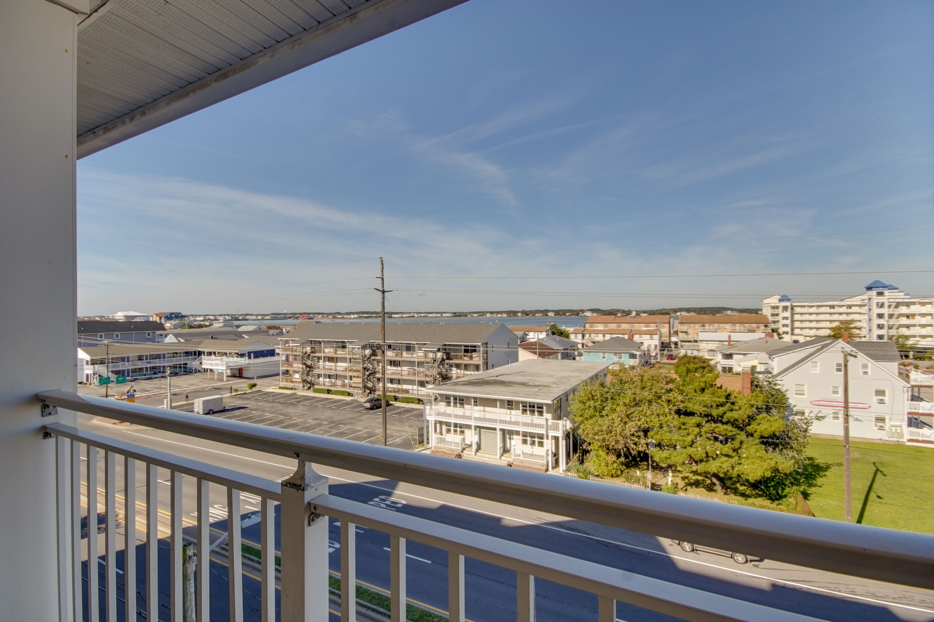 Une vue depuis un balcon donnant sur un parking, avec des bâtiments et un ciel dégagé.