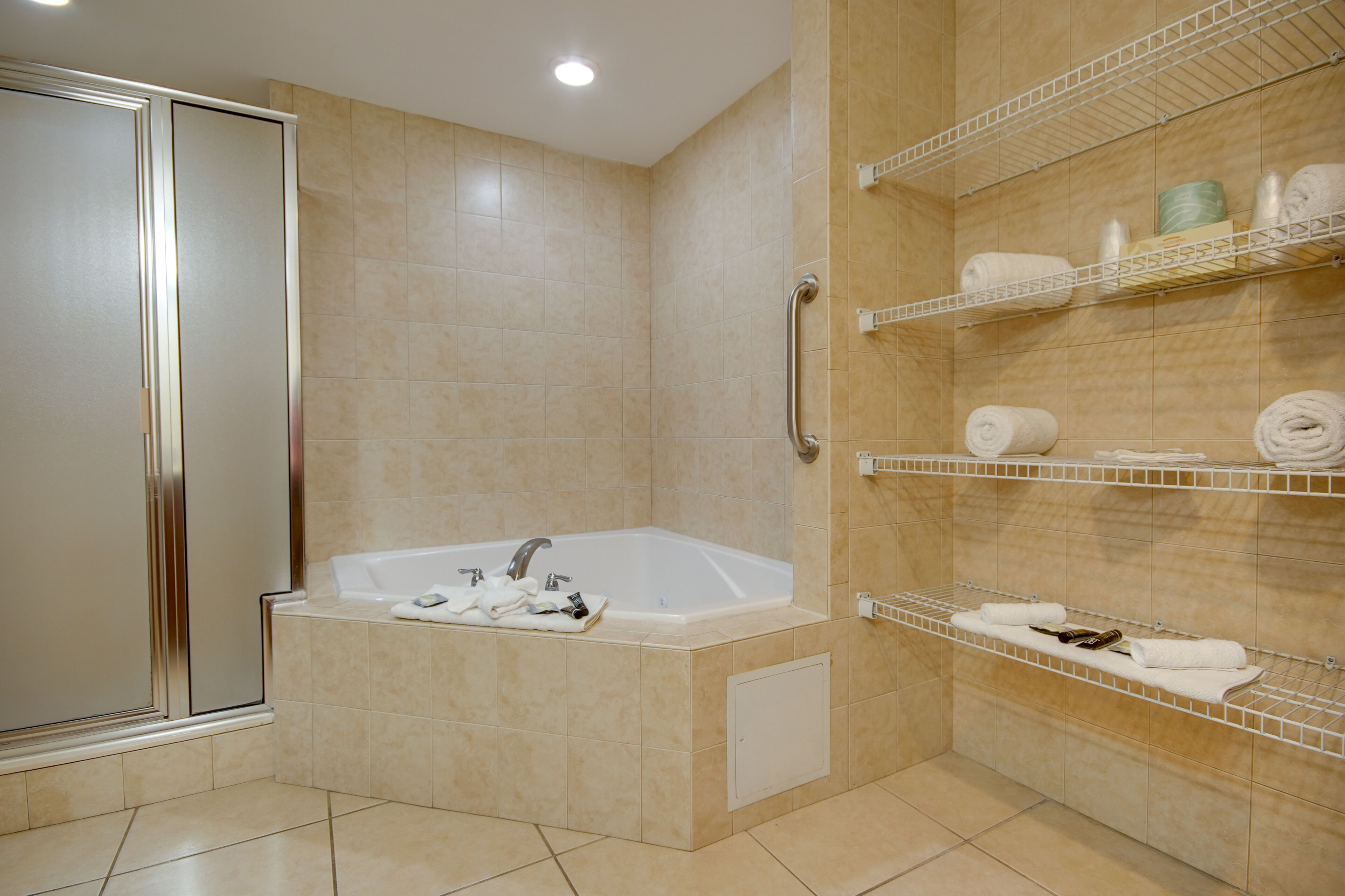 Een badkamer met een inloopdouche, een bad en planken met handdoeken en toiletartikelen.