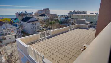 A rooftop terrace with a tiled floor, surrounded by residential buildings with balconies and a clear view of the ocean.