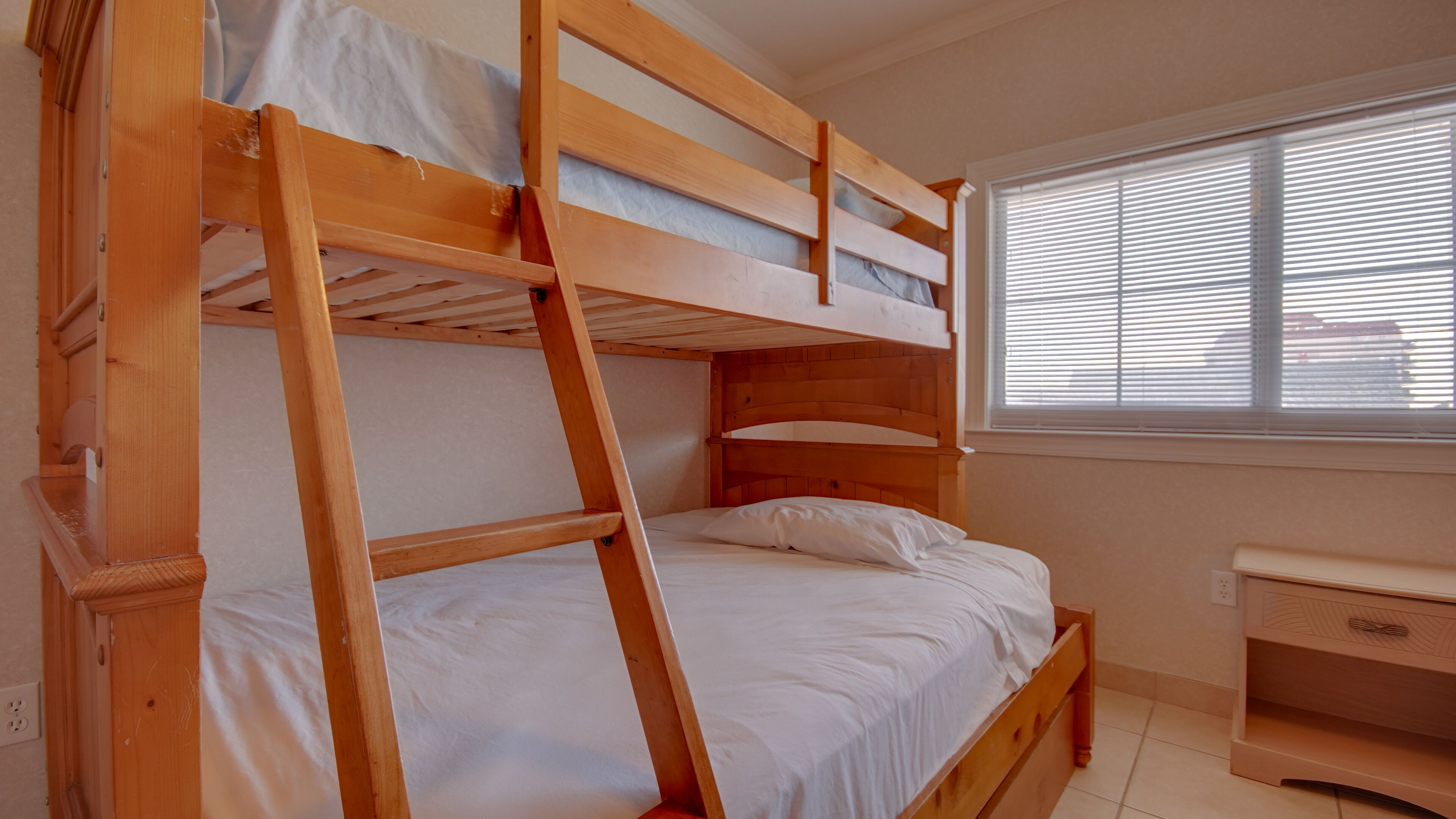 A bunk bed with a ladder, a small desk, and a window with blinds.
