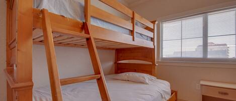 A bunk bed with a ladder, a small desk, and a window with blinds.