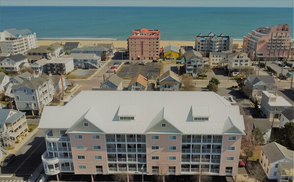 A coastal residential area with multi-story buildings, a beach in the background, and a parking lot in the foreground. - Americana Condos 10th street (Ocean City)