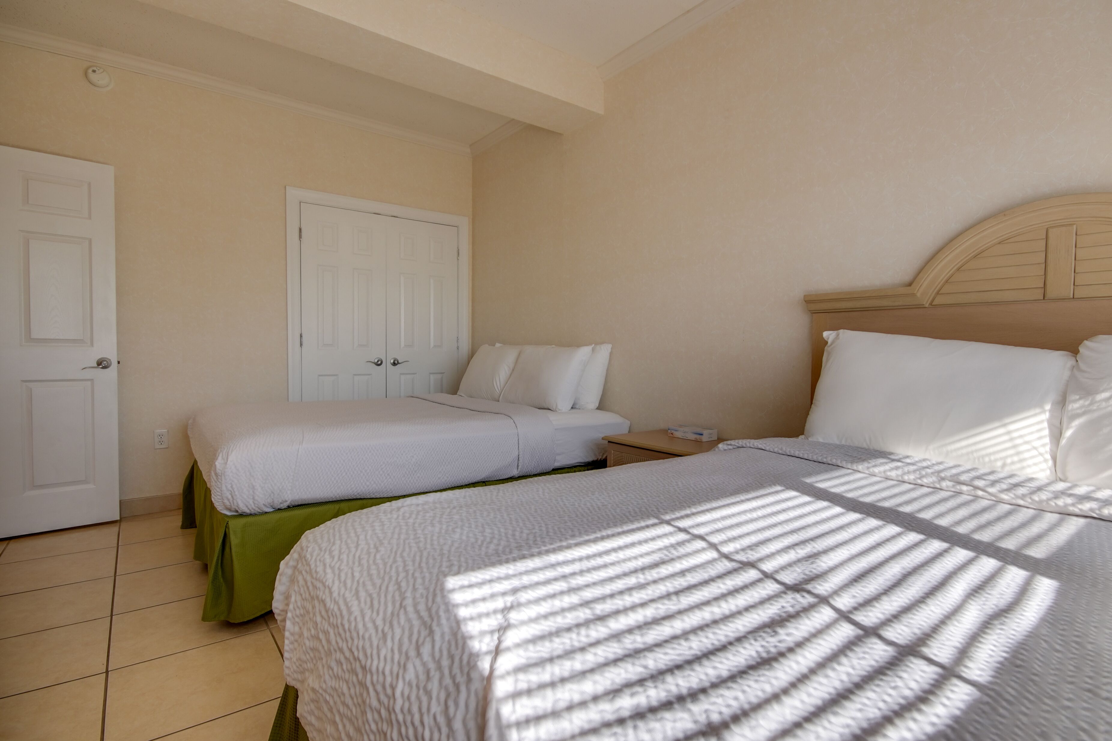 A hotel room with two beds, a wooden headboard, and a green skirted bed.