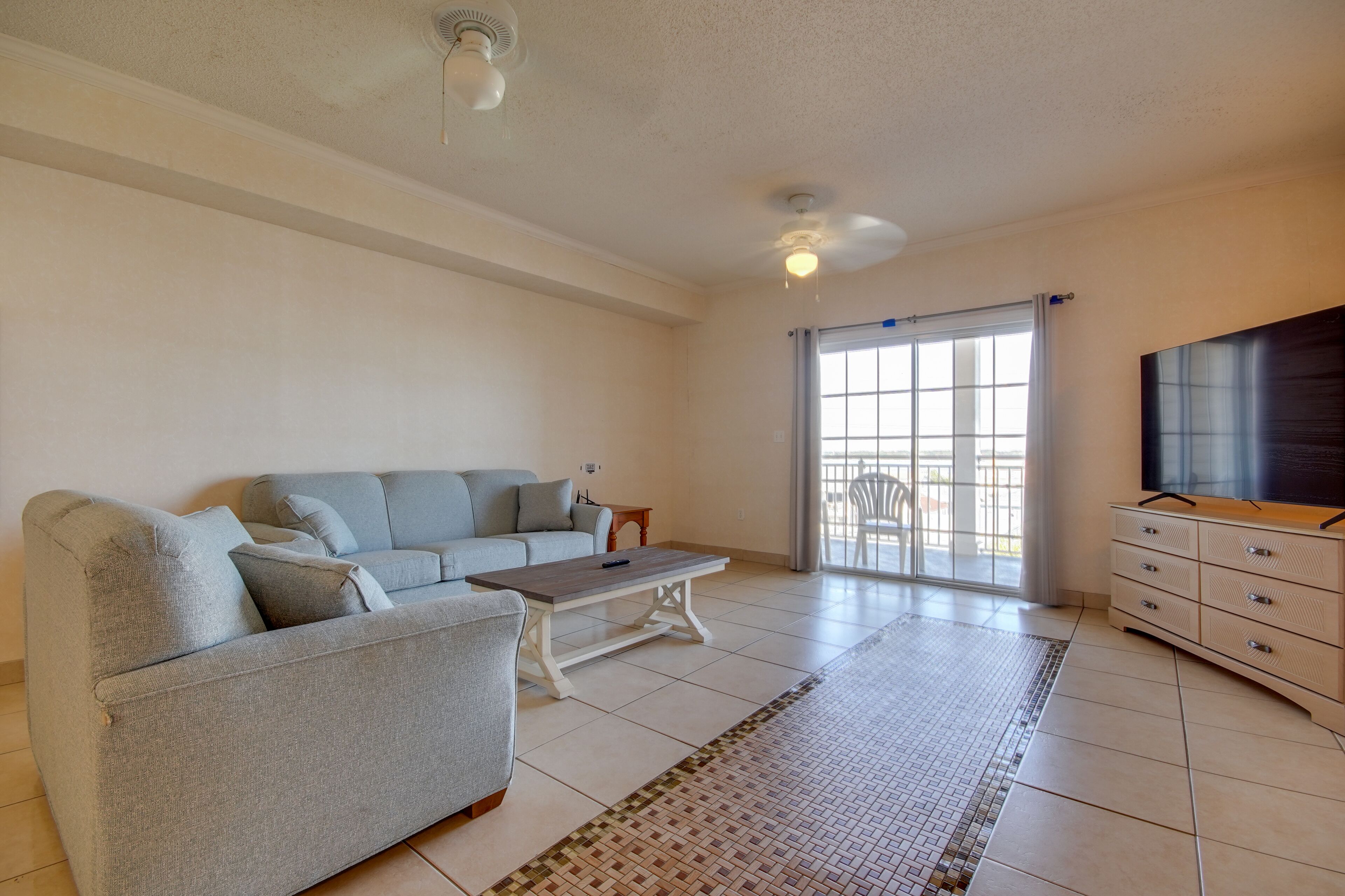 A spacious living room with a grey sofa, a wooden coffee table, and a TV on a wooden cabinet.