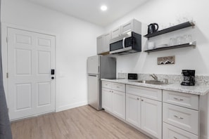 A modern kitchen with white cabinetry, a stainless steel refrigerator, a microwave, and a coffee maker.