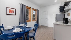 A dining area with a table set for four, a kitchen with a coffee maker, and a door leading to another room. - EV Charging. Private garage in town by restaurants (Mammoth Lakes)