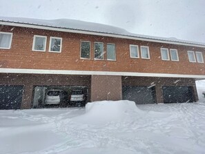 A building with multiple garage doors, a parked car, and a large snow accumulation in front.