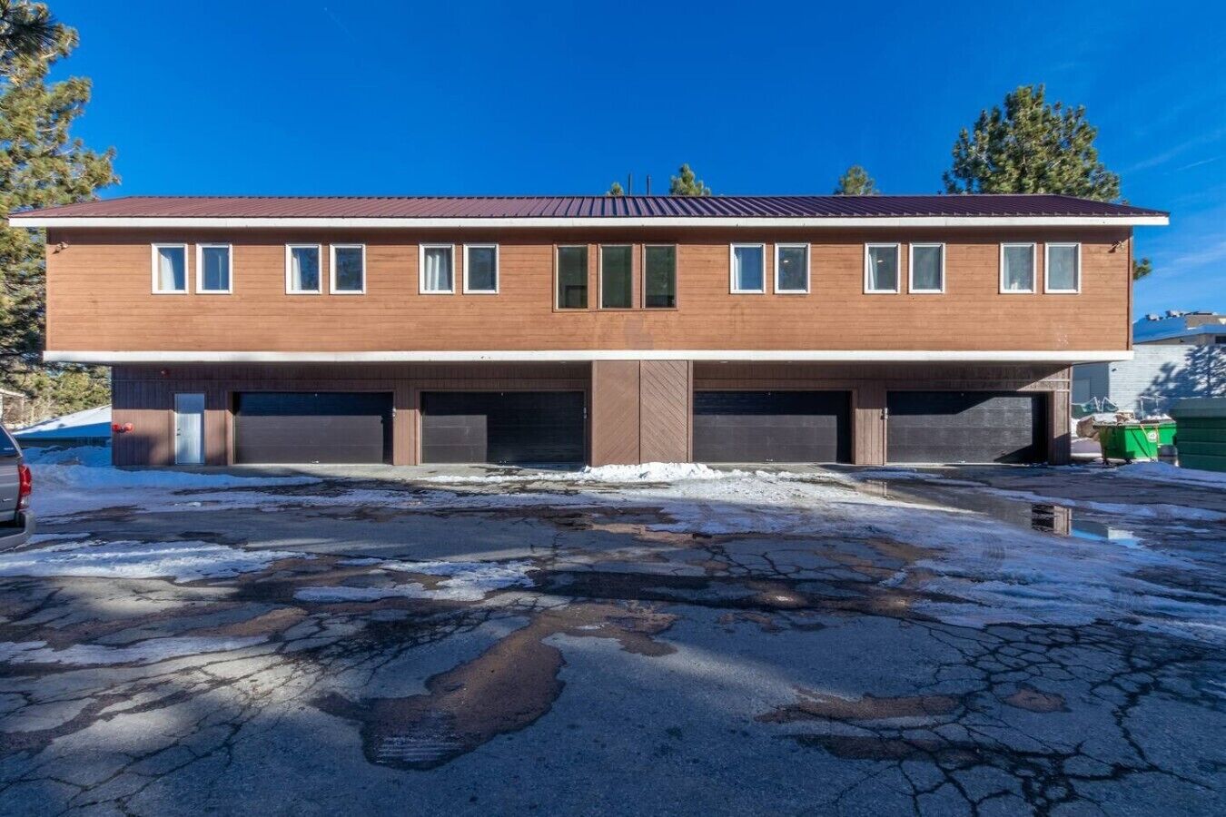 Un bâtiment à deux étages, doté d’un toit plat, de plusieurs portes de garage et d’un espace de stationnement présentant des fissures visibles et des plaques de neige.