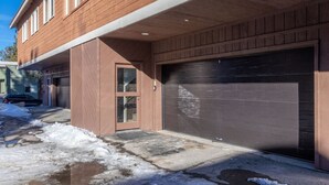 A residential building with a garage, a front door, and a driveway with snow.