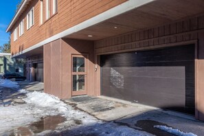 Een woongebouw met een garage, voordeur en een oprit met sneeuw.