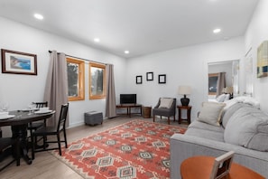 A living room with a sofa, a TV, a dining table with chairs, and a patterned rug.
