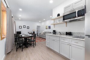 A modern kitchen with white cabinets, a microwave, a coffee maker, and a dining area with a table and chairs. - EV Charging, Quick access to slopes,  restaurants. (Mammoth Lakes)