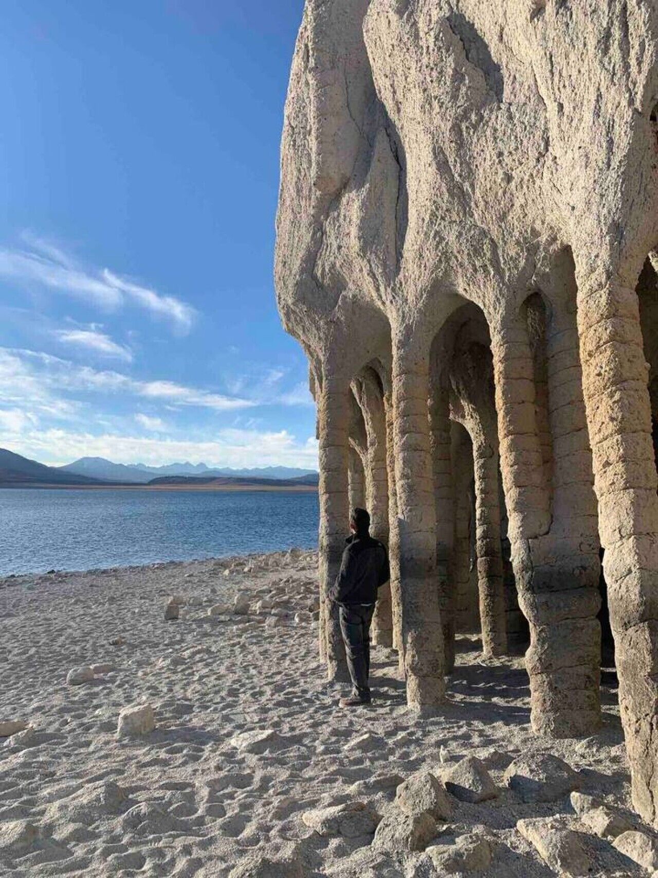 A person standing near ancient rock formations by a body of water.