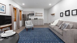 A modern living room with a grey sofa, a blue patterned rug, a TV, and a dining area with a table and chairs. - Private Garage, EV Charging By Restaurants &Shops (Mammoth Lakes)