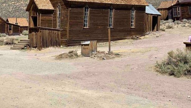 A wooden building with a bell tower, a front porch, and a dirt ground. - Private Garage, EV Charging By Restaurants &Shops (Mammoth Lakes)