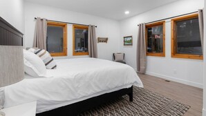 A bedroom with a bed, two windows with curtains, a bedside table, and a rug. - Private Garage, EV Charging By Restaurants &Shops (Mammoth Lakes)