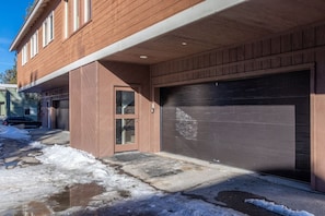 A residential building with a garage, a front door, and a driveway with snow.
