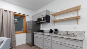 A compact kitchen with a refrigerator, microwave, coffee maker, and a wooden shelf above the sink. - Private Garage, EV Charging By Restaurants &Shops (Mammoth Lakes)