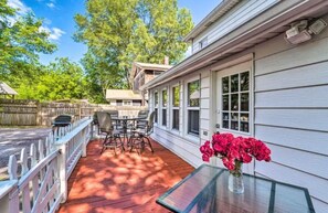 Enjoy al fresco dining on the covered patio with a dining table and chairs, surrounded by lush trees and a wooden fence.
