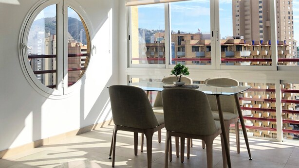 A modern living room with a large window, a dining area with a glass table, and a view of the cityscape. - Cristian's Apartment 2 (Benidorm)