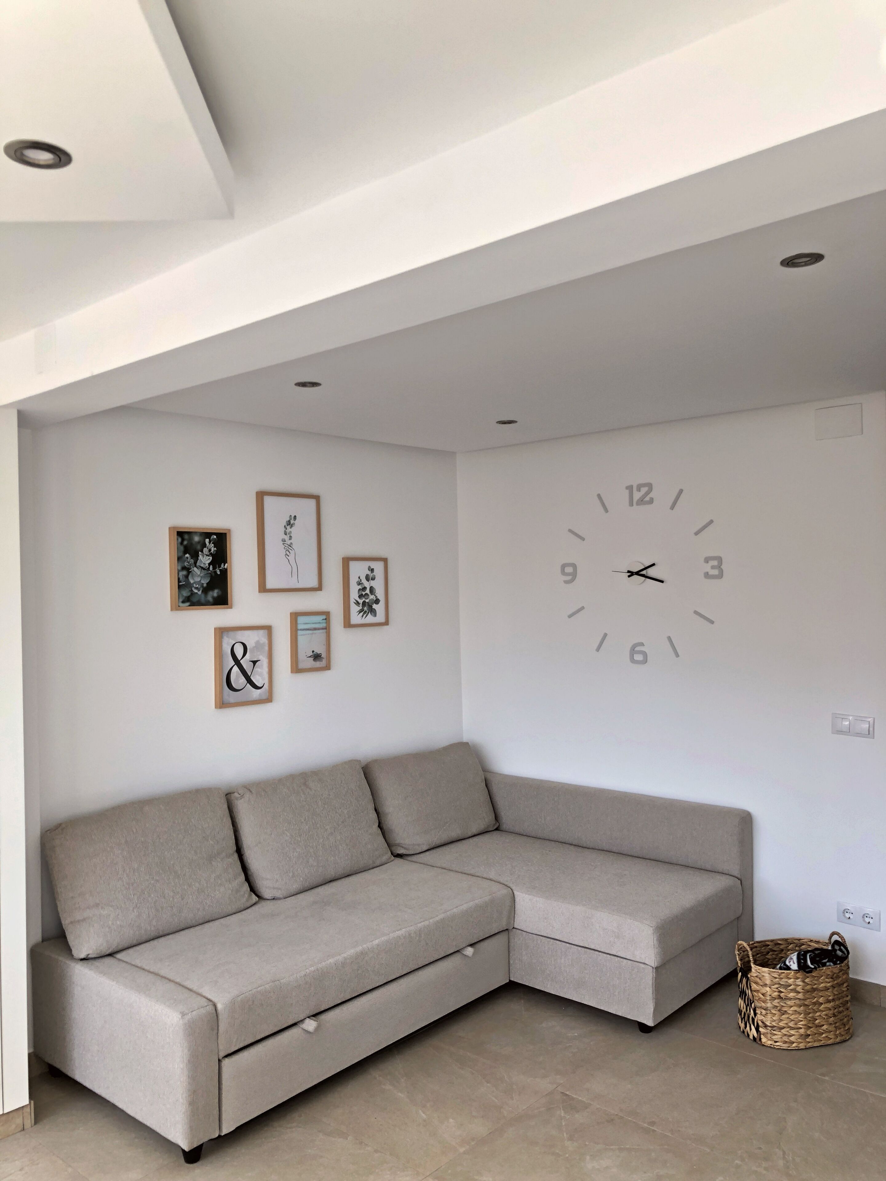 Un salon moderne avec un canapé d’angle beige, une horloge murale et des œuvres d’art encadrées.
