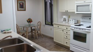 A compact kitchen with a sink, a dining table with chairs, a window with curtains, and a stove. - 2bd, 2ba, 1st Floor Condo: Pool, Short Drive to Beach, Tennis, Lanai, Near IMG (Bradenton)