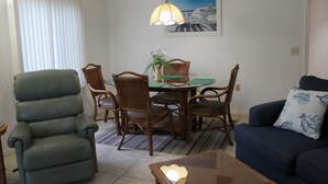 A living room with a green recliner, a blue sofa, a dining table with chairs, and a hanging lamp. - 2bd, 2ba, 1st Floor Condo: Pool, Short Drive to Beach, Tennis, Lanai, Near IMG (Bradenton)