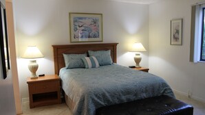 A bedroom with a bed, two bedside lamps, a nightstand, a black ottoman, and two framed pictures on the walls. - 2bd, 2ba, 1st Floor Condo: Pool, Short Drive to Beach, Tennis, Lanai, Near IMG (Bradenton)