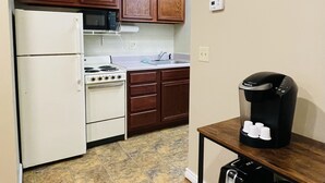 Cocina con refrigerador, estufa, microondas y armarios de madera. Hay una cafetera sobre una mesita.