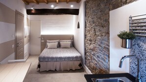 A bedroom with a bed, a built-in wardrobe, a stone wall, and a small kitchen area with a sink and a potted plant. - "Sea Drops" (CITR: 011024-CAV-0119) (Riomaggiore)