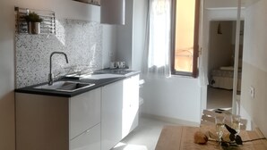 A kitchen with a stone wall, a wooden ceiling, and a window with curtains. - "Sea Drops" (CITR: 011024-CAV-0119) (Riomaggiore)