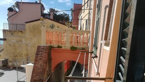 A narrow stairway leading to a balcony with a wrought iron railing and a small bridge over a drainage channel. - "Sea Drops" (CITR: 011024-CAV-0119) (Riomaggiore)