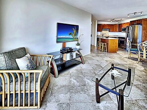Una sala de estar con sofá, mesa de centro, televisor y cocina al fondo.