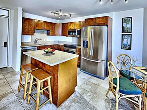A modern kitchen with wooden cabinets, a stainless steel refrigerator, a central island with stools, and a dining area with chairs and a table.