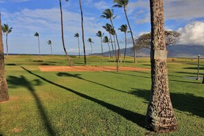 A golf course with a well-maintained green, sand bunkers, and tall palm trees. - Where Ocean Meets Pool Kihei Fully Upgraded Condo Stunning Views and Lanai (Kihei)