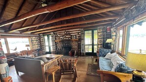 A rustic cabin interior with wooden furniture, a stone fireplace, and a large window.