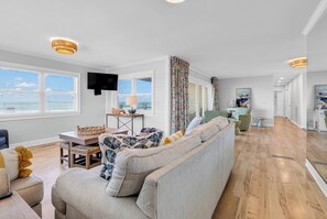 Ein geräumiges Wohnzimmer mit einer Couch, einem Fernseher, einem Esstisch mit Stühlen und einer Küche im Hintergrund.