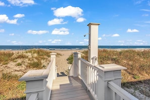 Eine Holzterrasse führt zu einem Strand unter blauem Himmel.