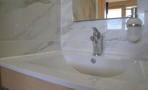 Een badkamer met een marmeren spatwand, een wastafel met een chromen kraan en een zeepdispenser.