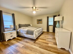 Een slaapkamer met een bed, nachtkastjes, een dressoir, een plafondventilator en een schilderij aan de muur.