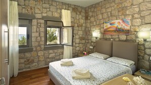 Un dormitori amb parets de pedra, un llit amb teles de llit florals, una finestra amb cortines i un quadre a la paret.