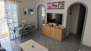 Ett vardagsrum med en tv, ett matbord, stolar, ett vitt soffbord och en takfläkt.
