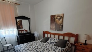 Un dormitorio con cama, cómoda, silla, escritorio, espejo, ventilador y una pared con un cuadro.