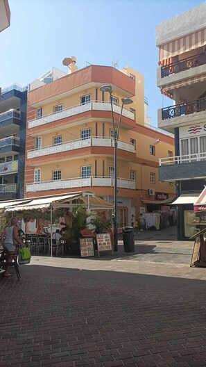 A multi-story building with balconies, a street vendor area, and a brick pavement.