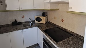 Ett kompakt kök med vita skåp, en mikrovågsugn, en diskho och en spis.
