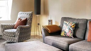 A living room with a patterned armchair, a grey sofa with colorful pillows, and a floor lamp.
