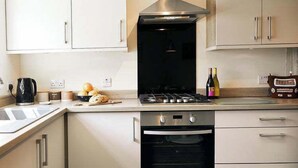 A modern kitchen with white cabinets, a stainless steel range hood, a sink, and an oven.
