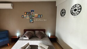 A bedroom with a bed, two bedside tables with lamps, a blue chair, and a wall with framed pictures and clocks labeled "Tavard de France" and "Paris". - Hibiscus beach and pool Sainte-Luce Martinique (Sainte-Luce)