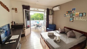 A hotel room with a bed, a TV, a desk, and a balcony with a table and chairs. - Hibiscus beach and pool Sainte-Luce Martinique (Sainte-Luce)