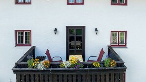 Um edifício branco com varanda, que apresenta uma mesa, duas cadeiras e arranjos florais.